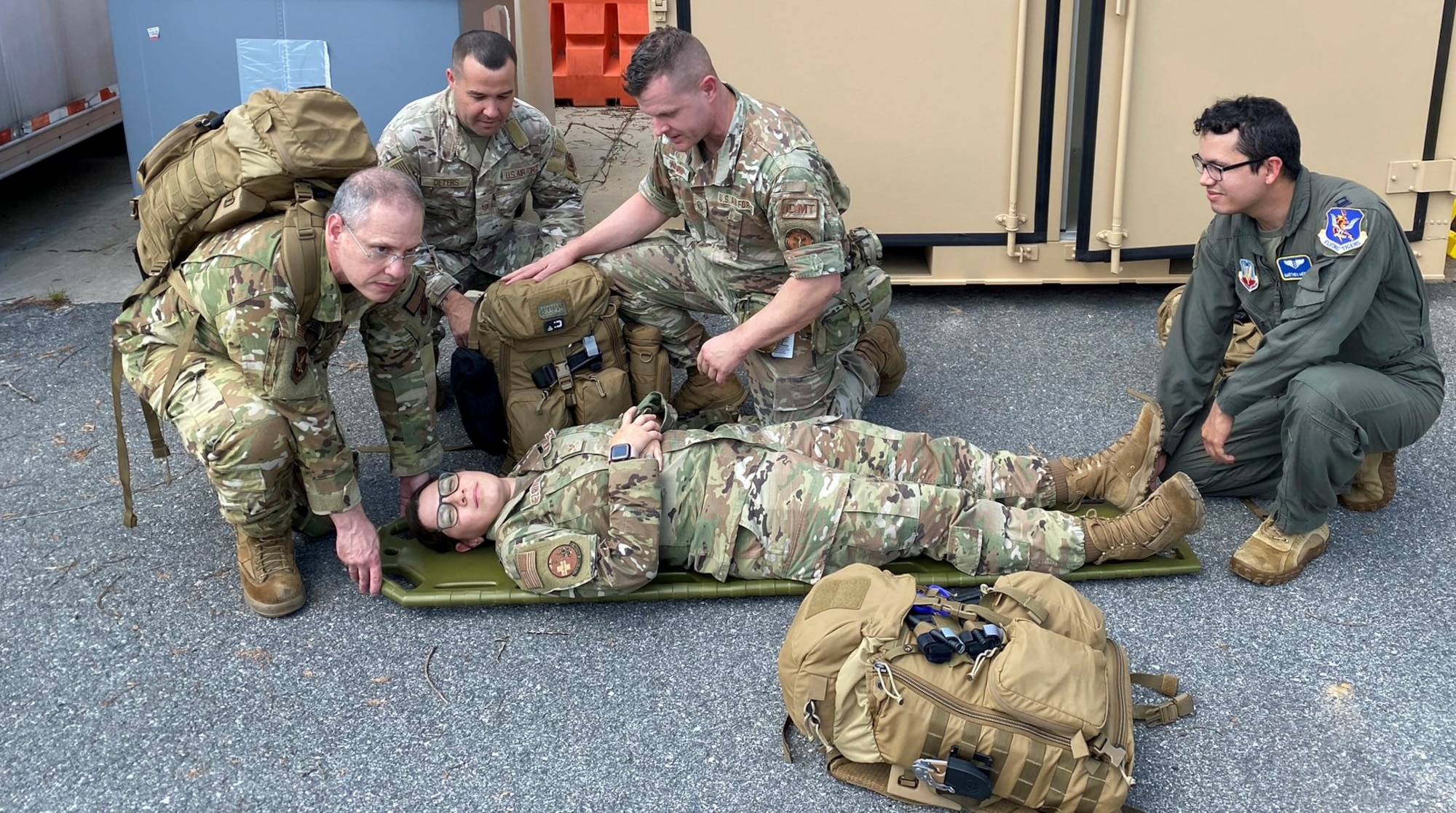 A photo of medics squatting next to a person on a stretcher, or litter.
