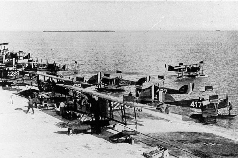 Several seaplanes sit on a beachhead or nearby in the water.