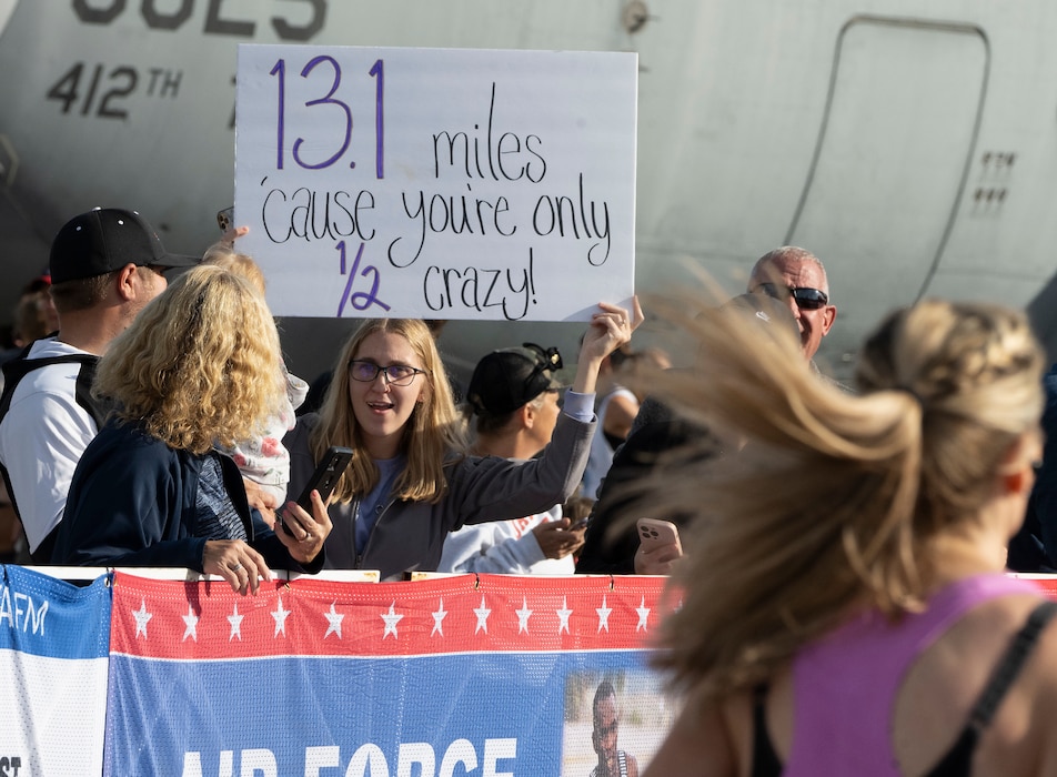 A woman holds up a sign that reads "13.1 miles 'cause you're only half crazy!