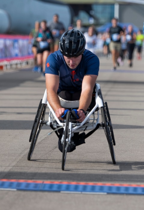 A man in a 3-wheeled racing wheelchair approaches a blue line on the ground.