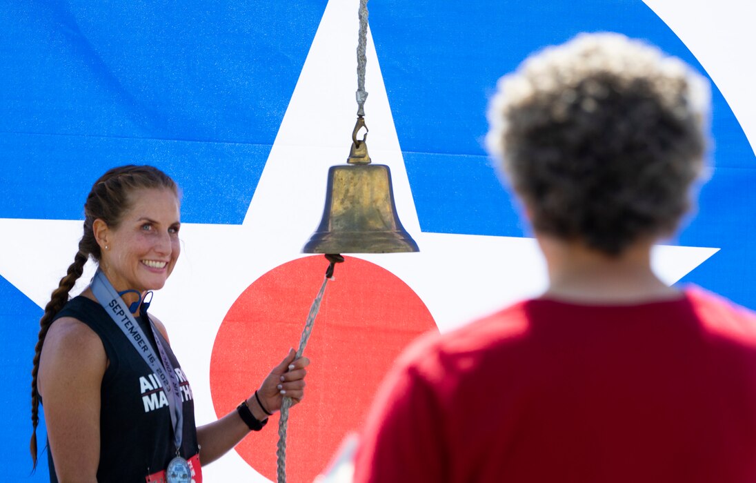 A woman with a long ponytail stands with her hand on a bell's lanyard.