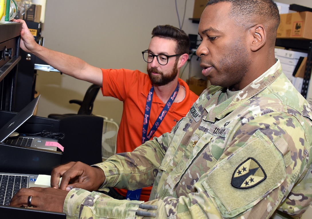 Maj. Brandon McCalla, a signal officer with U.S. Army Reserve Sustainment Command’s Detachment 7, familiarizes himself with the information system interfaces at Army Medical Logistics Command headquarters during a recent training assignment at Fort Detrick, Maryland. Also pictured is Matt Tyler, desktop support lead for AMLC’s G-6. (C.J. Lovelace)