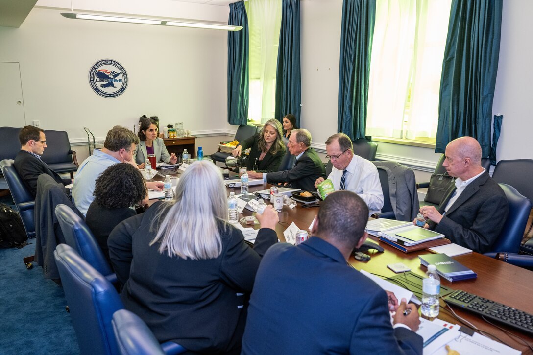 A group of men and women in civilian attire sit around a conference table.