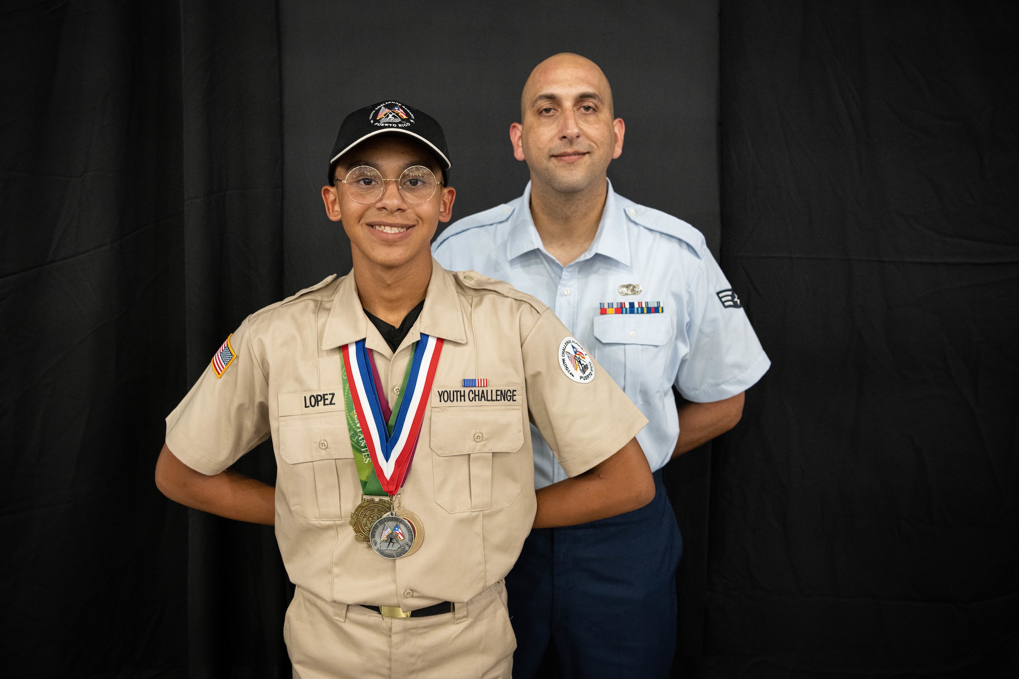 Cadet Jan Lopez with the Puerto Rico National Guard Youth ChalleNGe Academy, 3rd Platoon, Wolfpack, Class 23-02, poses for a photo with his father, U.S. Air Force Senior Airman Hector Lopez Rosa, a financial management technician with the 156th Comptroller Flight, Puerto Rico Air National Guard, during his graduation ceremony at Pontifical Catholic University of Puerto Rico, Ponce, Puerto Rico, Sept. 15, 2023. Jan Lopez received his high school diploma after completing the 22-week PRNG Youth ChalleNGe Academy program, where he studied for his high school diploma and also received vocational education from several career fields. (U.S. Air National Guard photo by 2nd. Lt. Eliezer Soto)