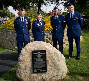 Four Airmen stand in front of a memorial plaque.