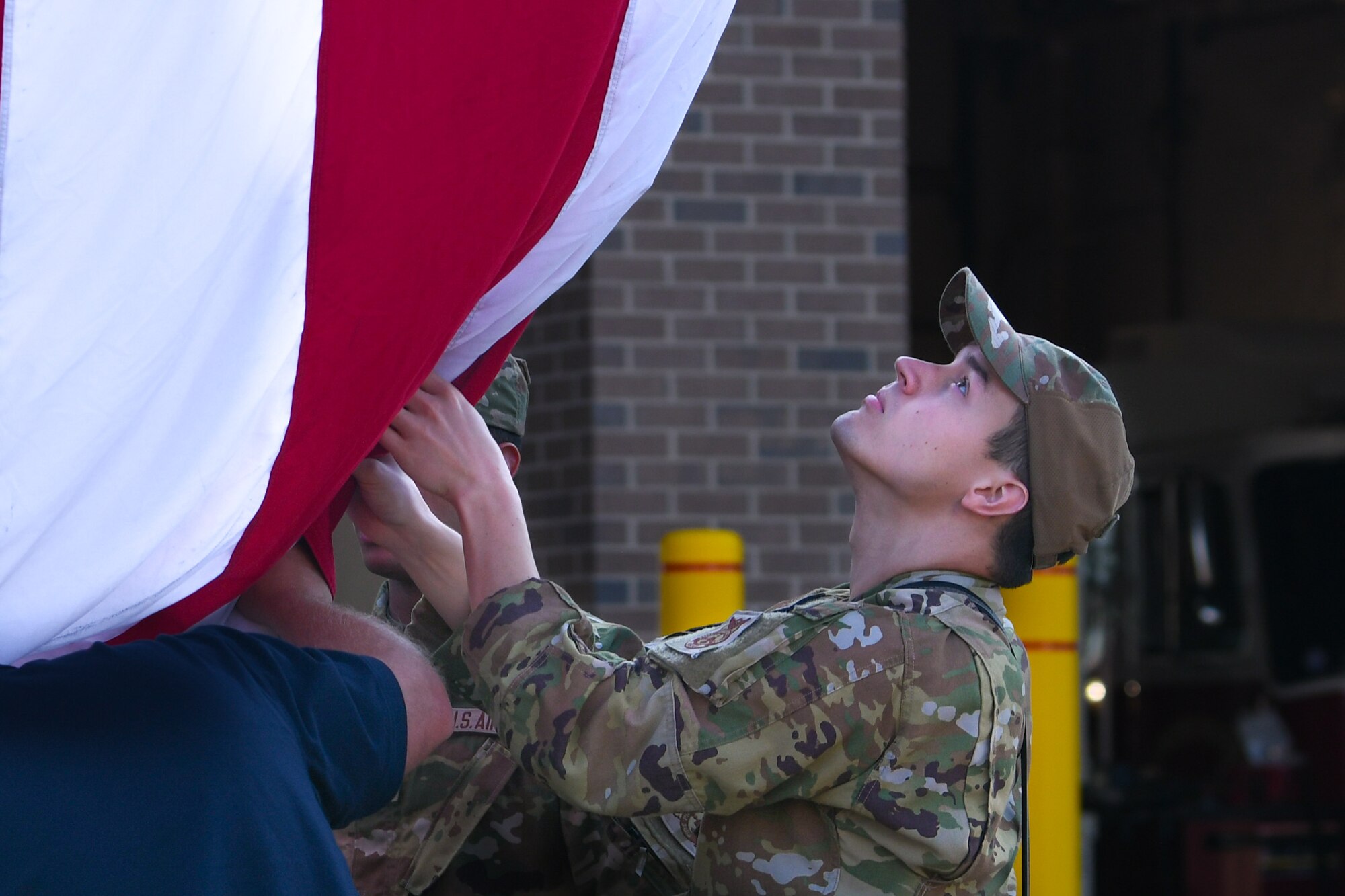Airmen assists wingmen in lowering the American flag and looks up at it.