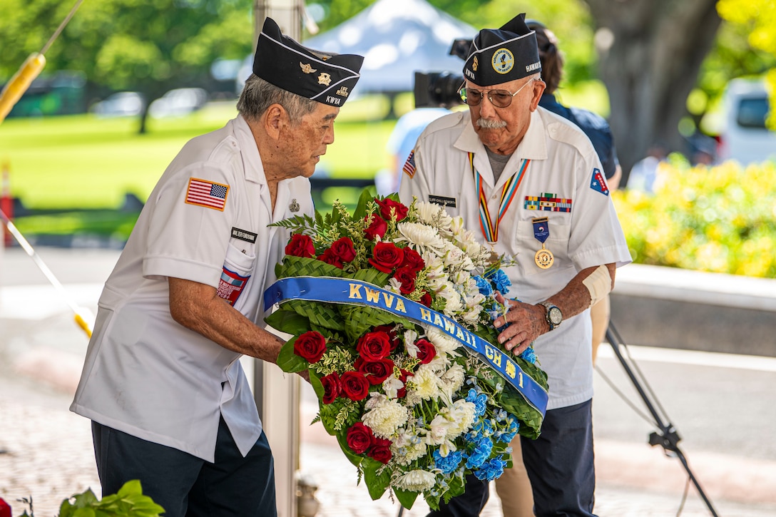 Two veterans hold a wreath covered with flowers.
