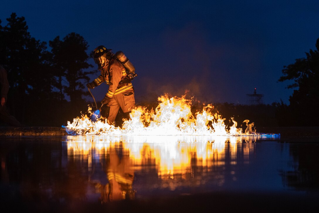 A Marine uses a torch to set a fire at night.