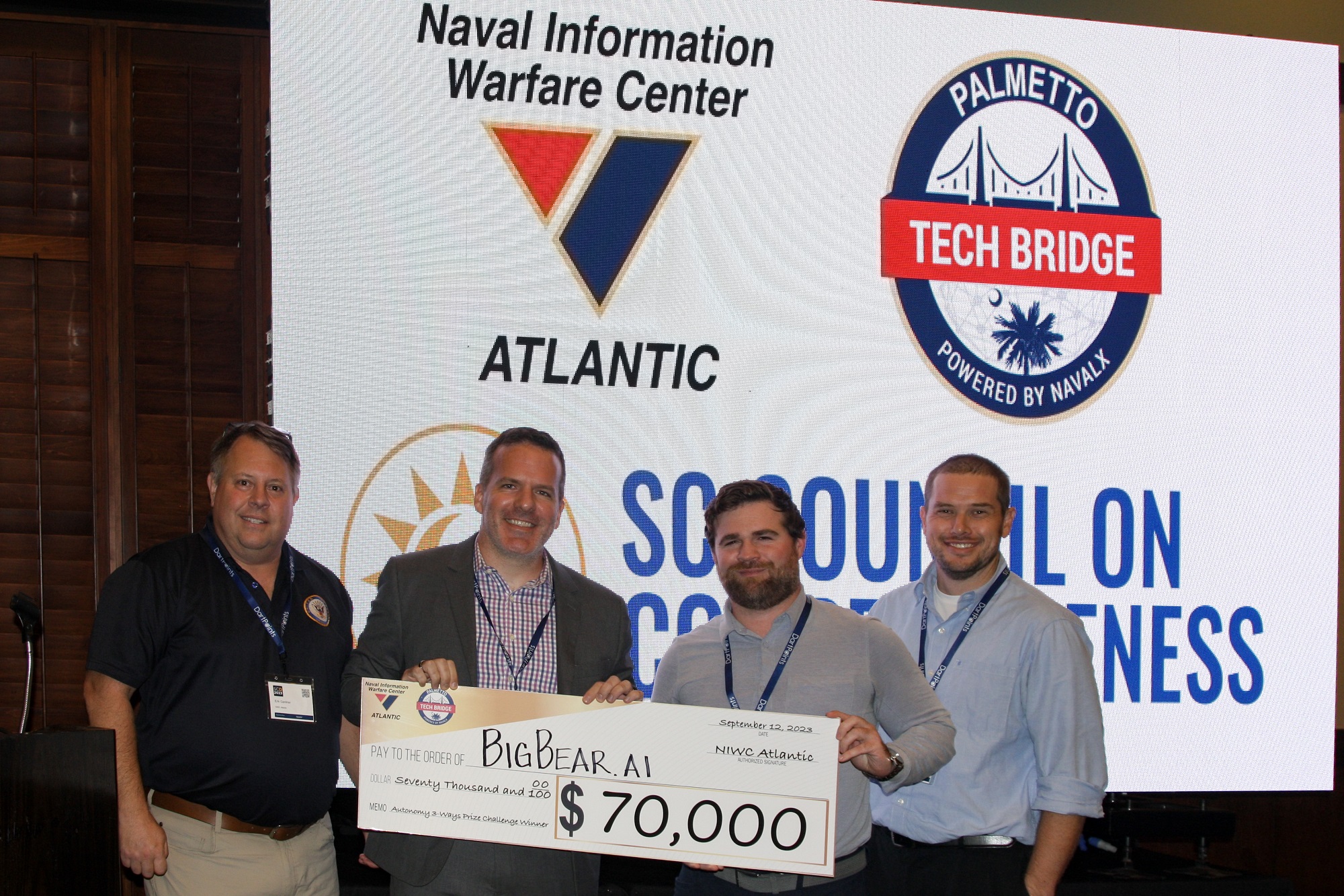 almetto Tech Bridge (PTB) Director Erik Gardner (left) and Dr. Luke Overbey (right), senior scientific technical manager for autonomy at Naval Information Warfare Center Atlantic, present a $70,000 cash prize to BigBear.ai on Sept. 12 at the 2023 SC Decoded Conference in Myrtle Beach for winning the PTB’s “Autonomy 3 Ways Prize Challenge.”