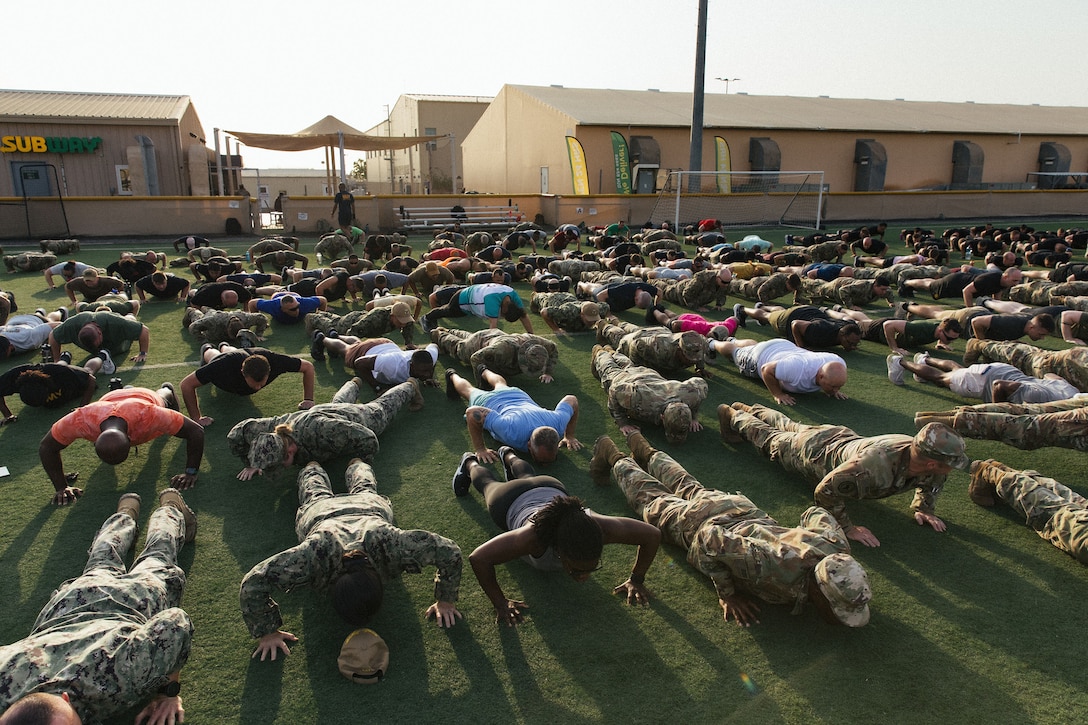 A large group of service members do pushups on a field.