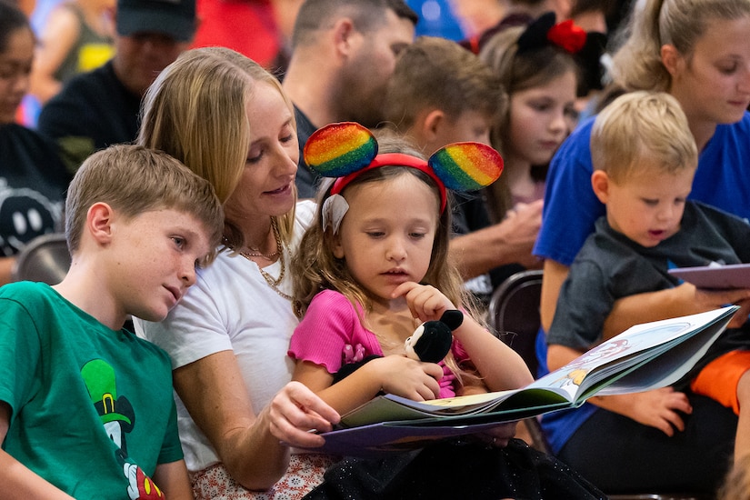 Seated adults read books to children seated beside them and in their laps.
