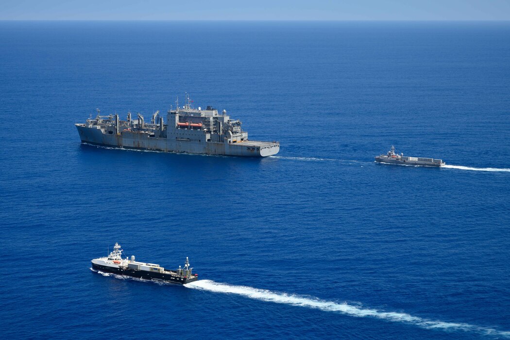 USNS Charles Drew (T-AKE 10) transits the Pacific Ocean with the unmanned surface vessels Ranger, top right, and Mariner.