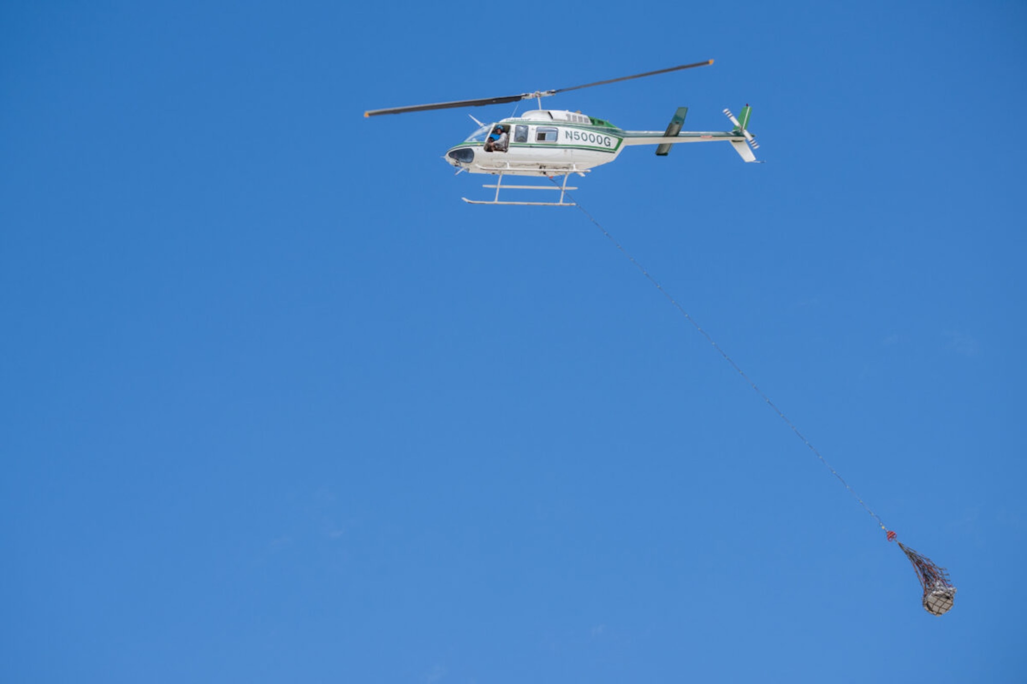 A photo of a helicopter carrying a capsule in a sling