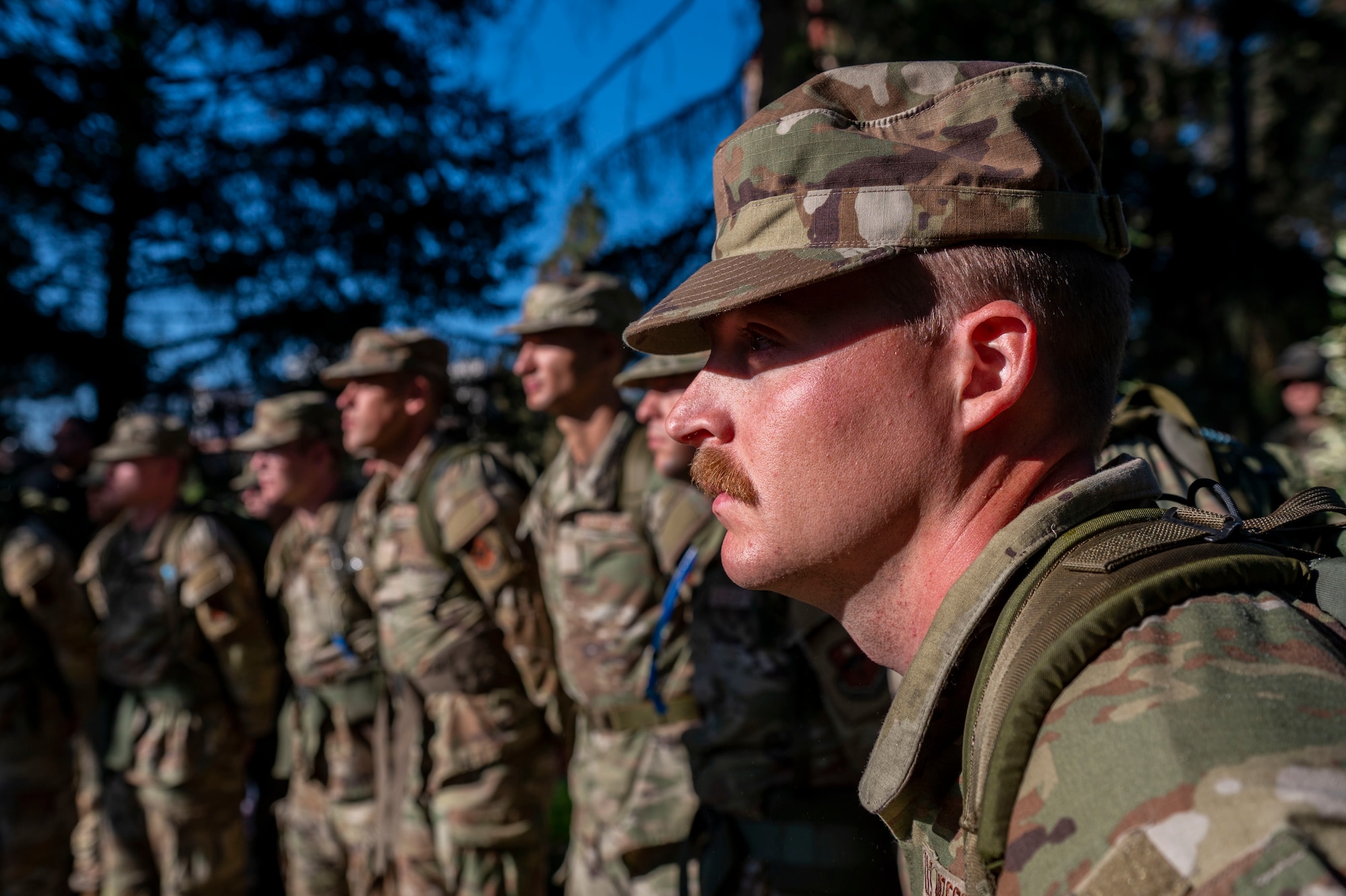 Airman 1st Class Keith Apostolos, a survival, evasion, resistance and escape candidate assigned to the 66th Training Squadron, stands in formation with fellow candidates while listening to opening remarks before a 24-hour ruck march at Riverfront Park in Spokane, Washington, Sept. 14, 2023. During the ruck march, Airmen from Fairchild Air Force Base kept the Prisoner of War/Missing in Action flag in constant motion to honor National POW/MIA Recognition Day. The ruck march began on Sept. 14 at the Vietnam Veterans Memorial in downtown Spokane and continued through Airway Heights before concluding at Fairchild AFB. The event culminated with a recognition ceremony on Sept. 15 to honor all American prisoners of war and those Americans still missing in action, as well as their families. Every year, the third Friday in September is recognized in the United States as National POW/MIA Recognition Day. The Department of Defense is steadfast in its commitment to finding, recovering, identifying and repatriating the remains of its heroes who are unaccounted for. (U.S. Air Force photo by Staff Sgt. Lawrence Sena)