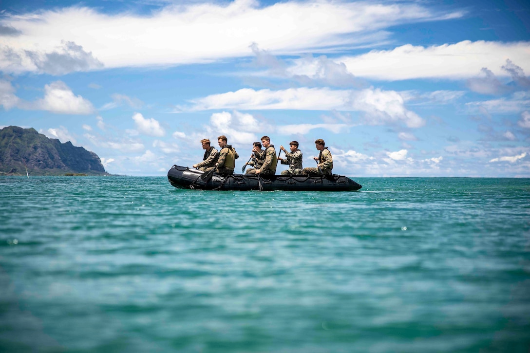 Marines paddle through a body of water in a rubber raft.