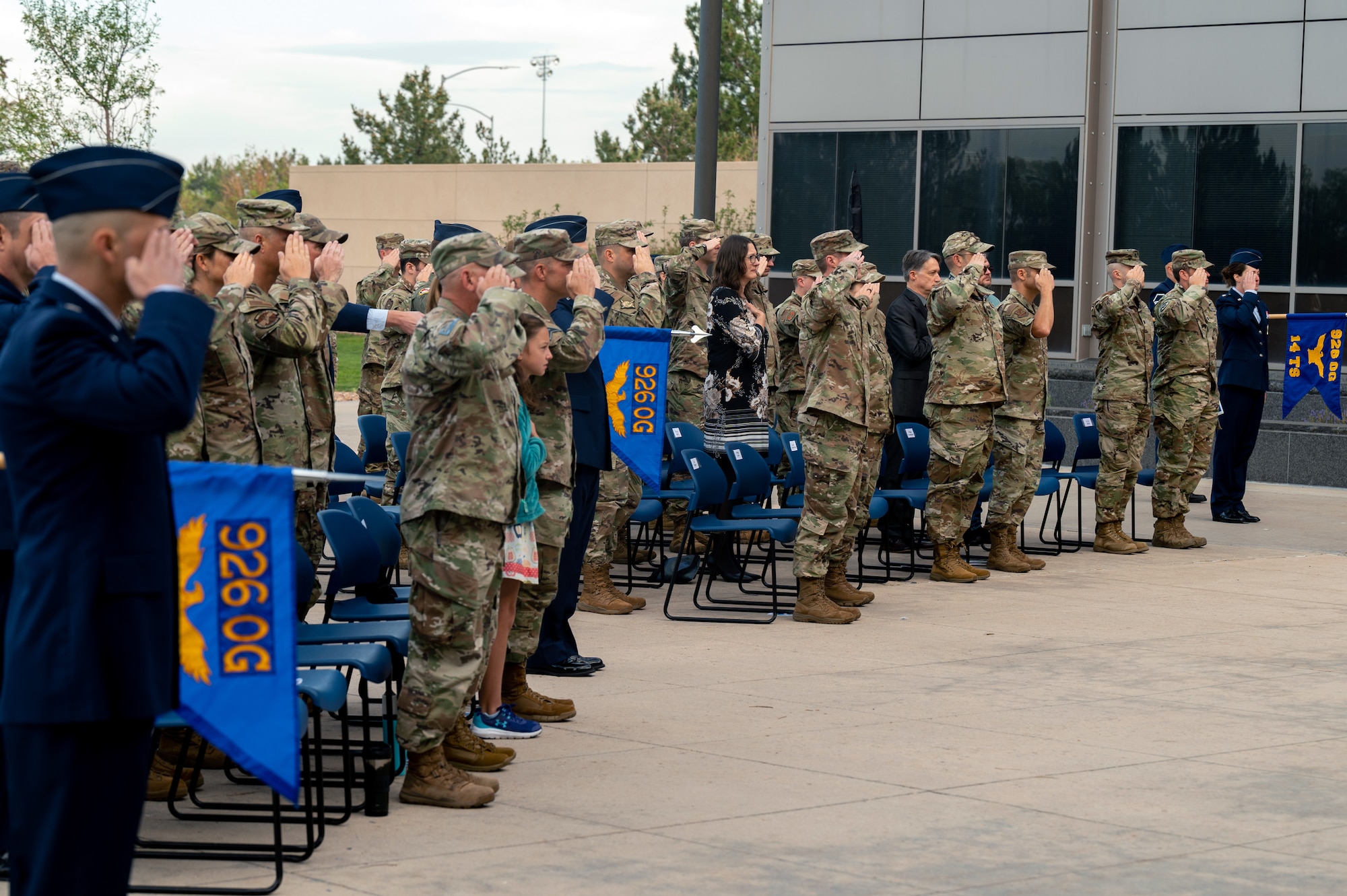 A group of people in military uniforms performing a salute outdoors near a building.