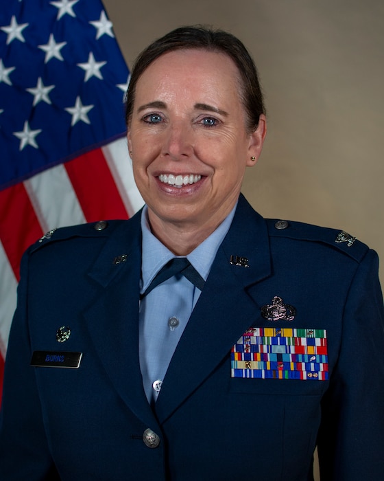 Service member smiles for official portrait in front of US flag wearing their service dress blues