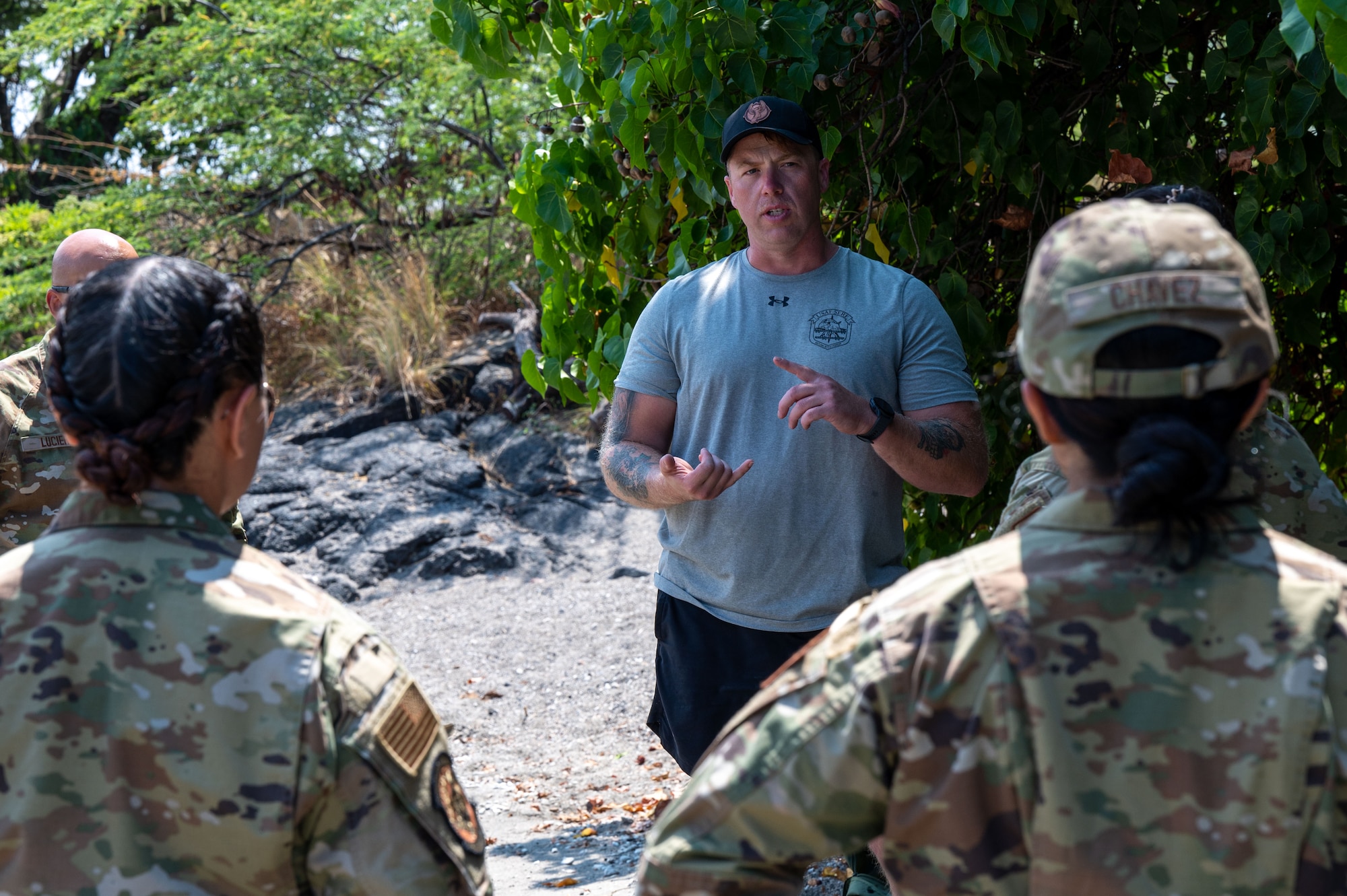 a man in a t-shirt talks to two people in military uniforms while standing on a sandy beach