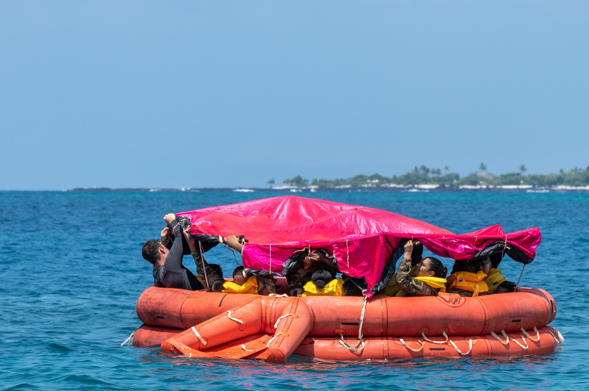 people in an orange life boat float in the water and hold a red canopy above them