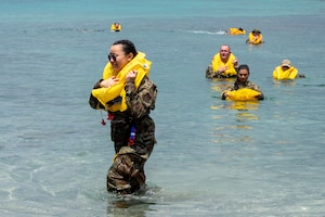 people in military uniforms wear life vests and swim to shore from the water