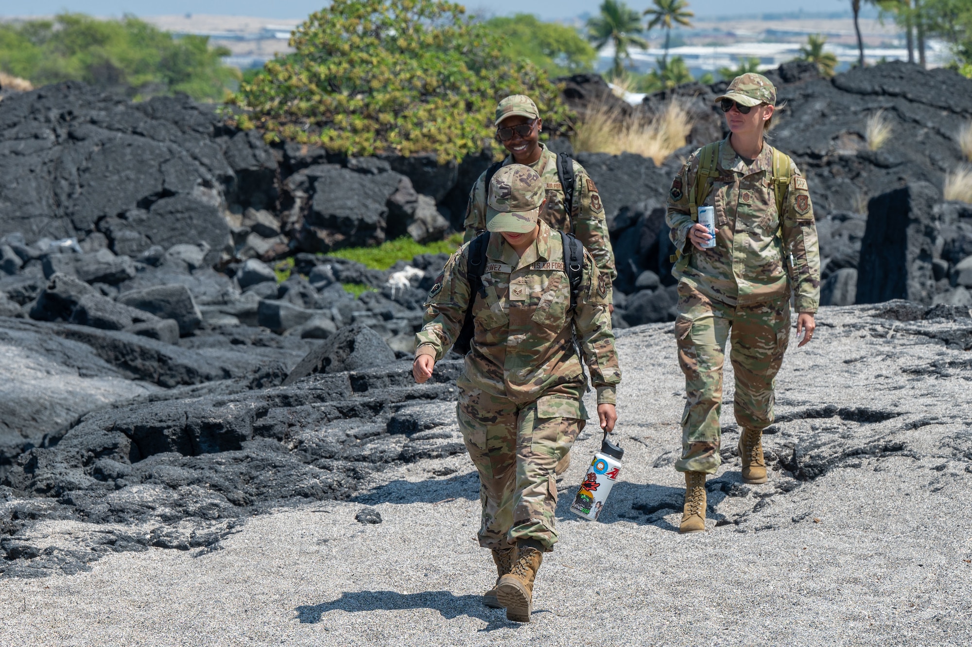 three people in military uniforms walk along a sandy beach