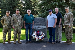 Attendees of the Outcome 54 and 55 commemoration ceremony stand in by a plaque with a wreath in front