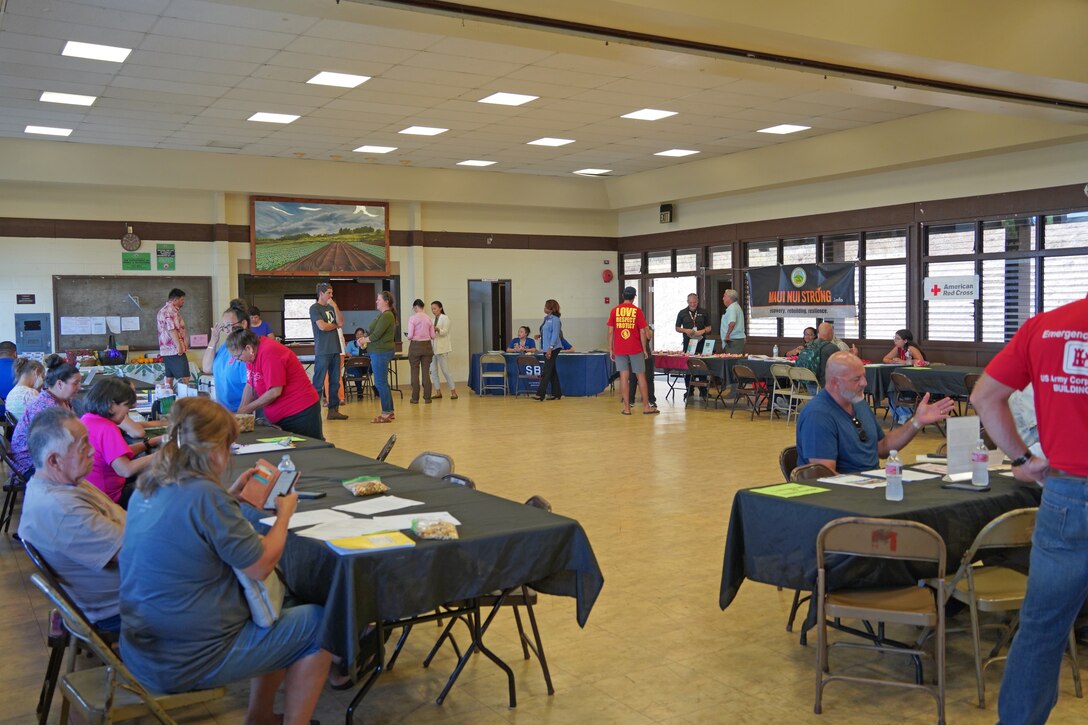 The image shows a large open room with several tables where people are seated to offer information