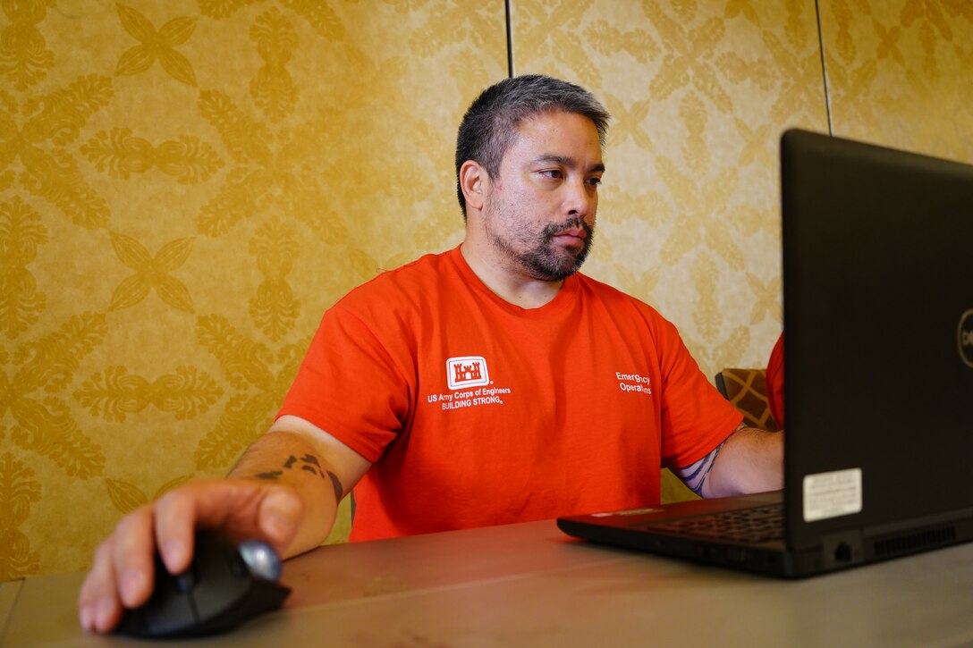 A man in an Army Corps of Engineers t-shirt works at a computer