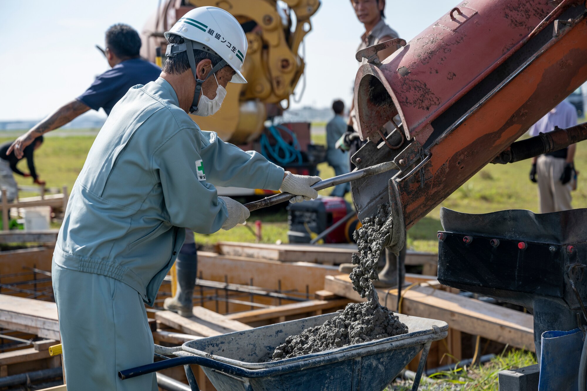 A Japanese man fills a wheelbarrow with wet cement.