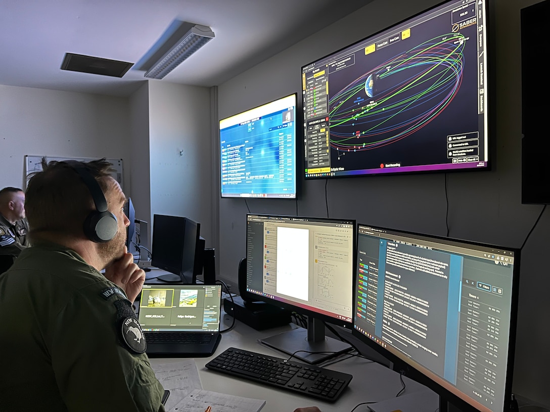 Man in uniform sitting at desk staring at four computer screens