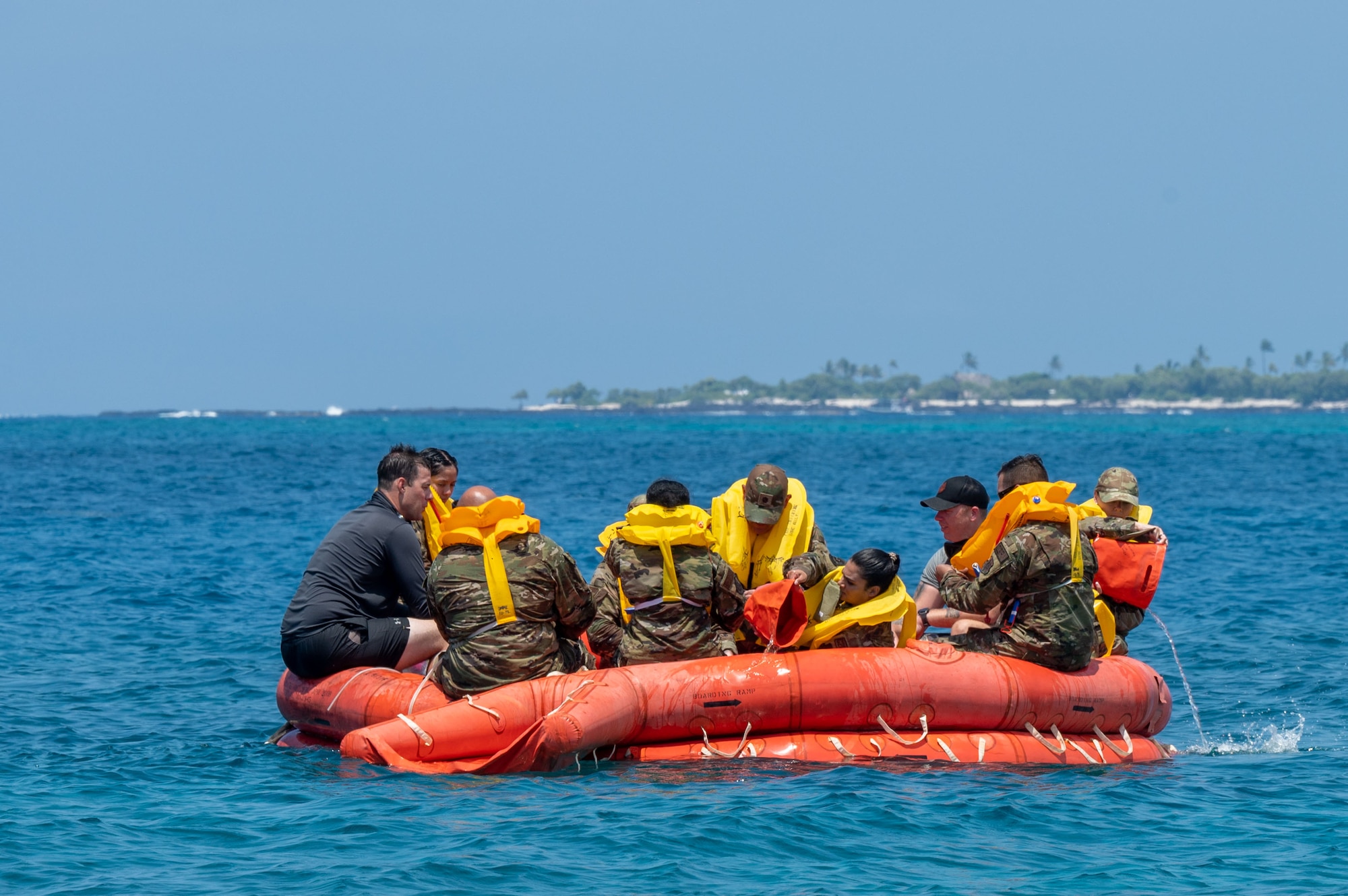 people in military uniforms and yellow life vests float in an orange life raft in the water