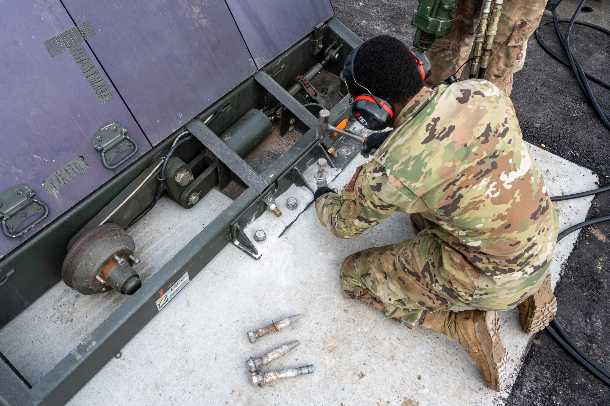 An Airman hammers a bolt into a concrete pad.
