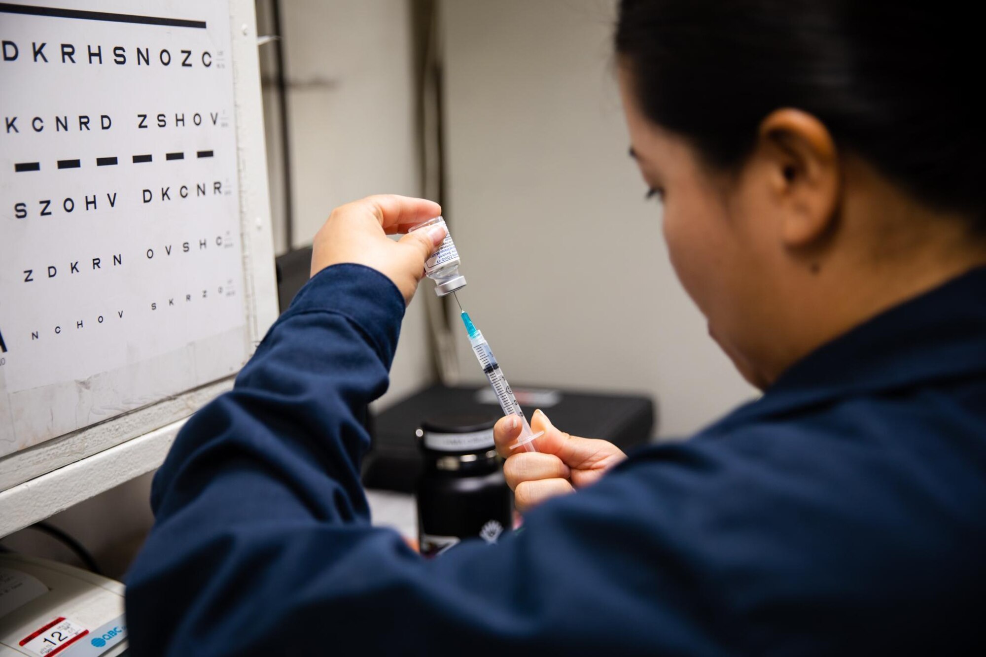 A U.S. Navy hospital corpsman draws a COVID-19 vaccine from a vial.