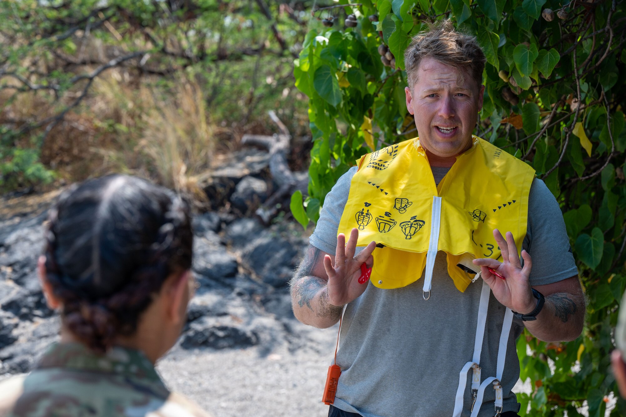 a man in a t-shirt and life vest stands on a sandy beach and talks to a person in a military uniform