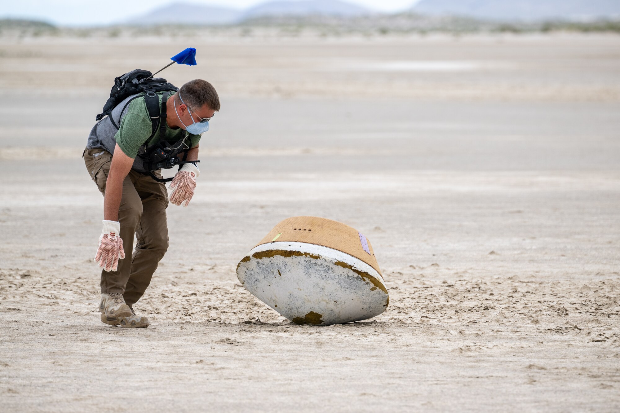 A photo of a man looking at a large, oval shaped recovery container laying in the desert.