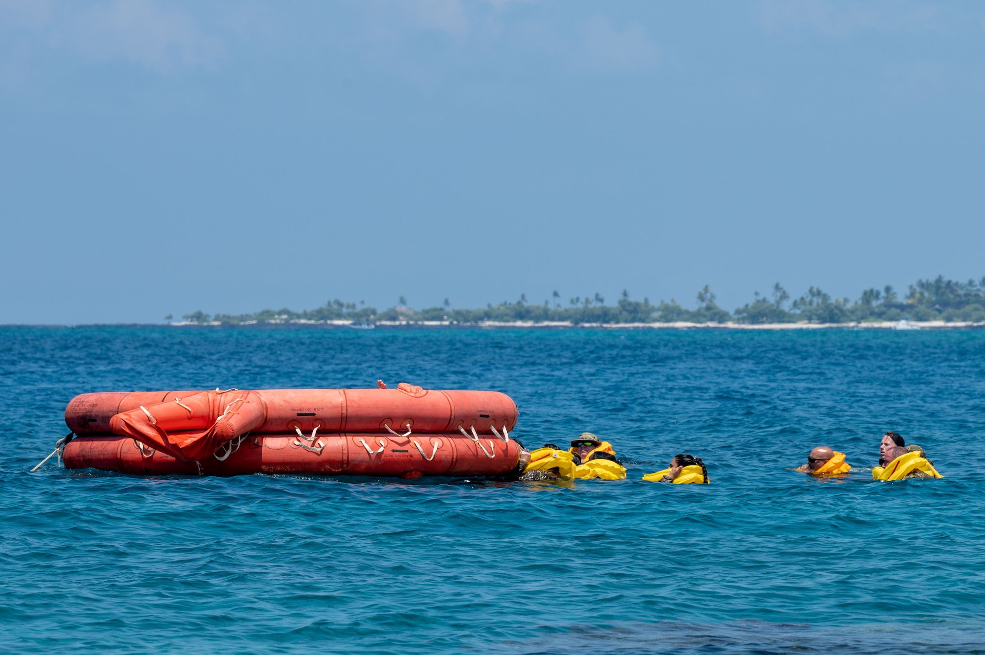 people in yellow life vests float in the water next to an orange life boat