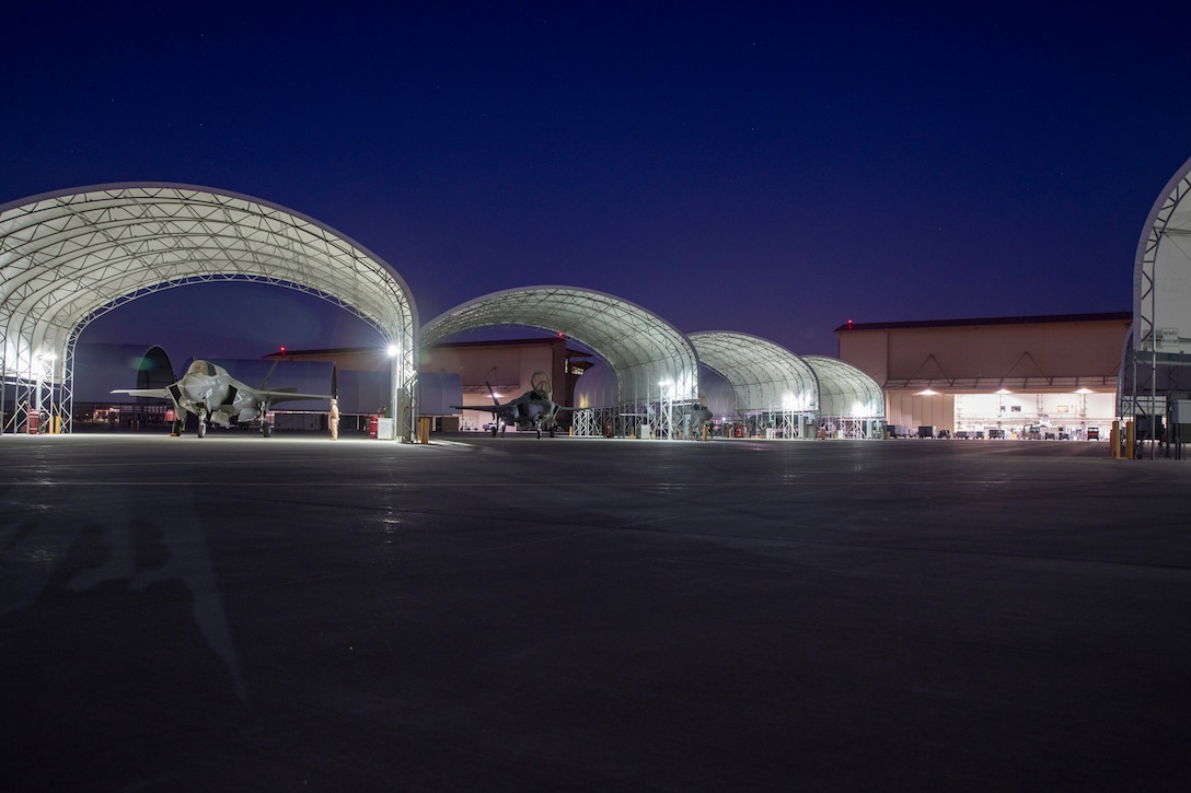 Fighter jets sit on the tarmac at night.