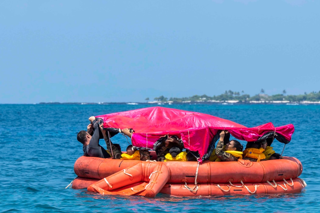 Airmen assemble a canopy over their heads while traveling through a body of water in a rubber raft.