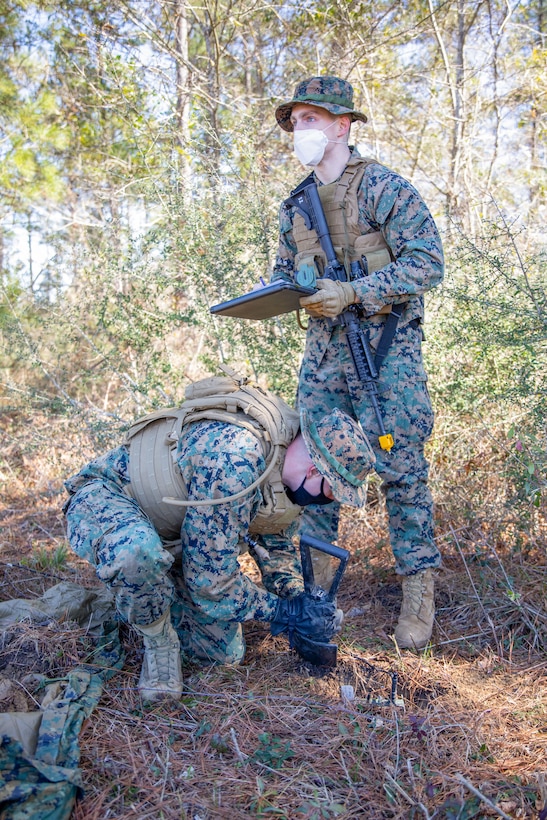 Lance Cpl. Corey Camphouse, a field radio operator for Battlespace Surveillance Company, conceals a ground sensor while Lance Cpl. Daniel Hance, an intelligence specialist for Battlespace Surveillance Company, plots the coordinates during a reconnaissance and surveillance field exercise on Camp Shelby, Miss., Feb. 19, 2021. This training develops and refines platoon and section patrolling and increases proficiency in ground sensor operations. (U.S. Marine Corps photo by Lance Cpl. Mitchell Collyer)