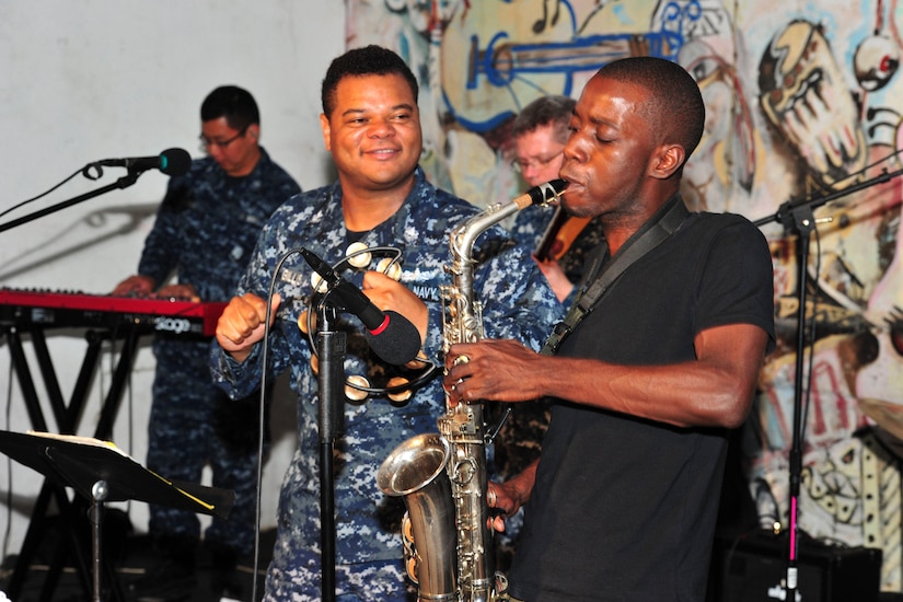 Military and civilian musicians play their instruments together.