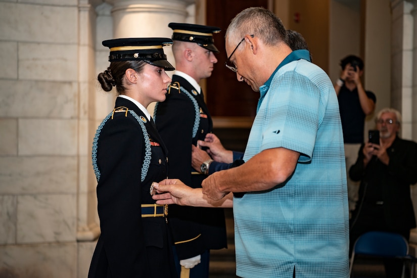 A man places a pin on a soldier's uniform.