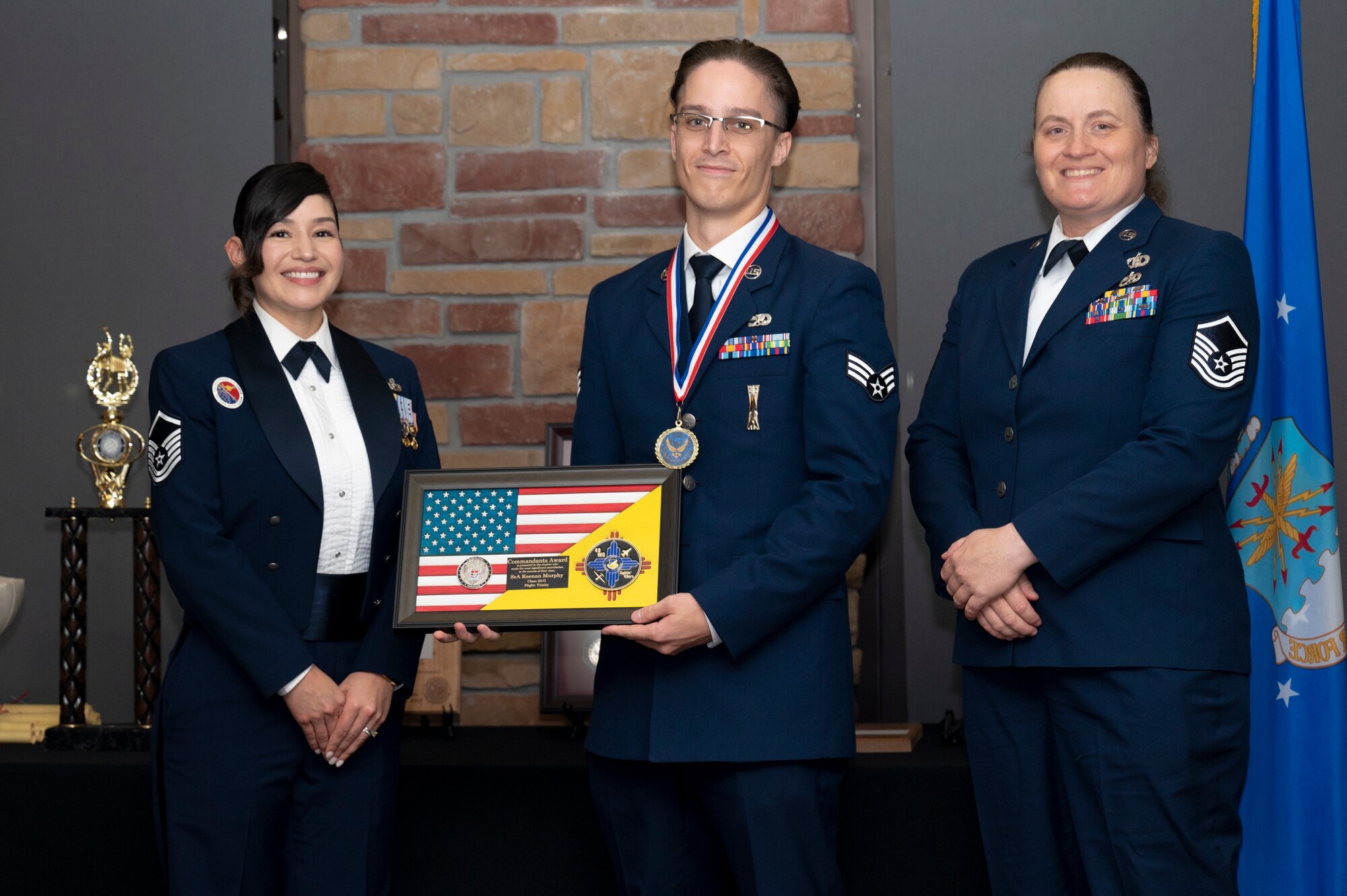 U.S. Air Force Senior Airman Keenan Murphy, center, Airman Leadership Graduate, accepts the Commandant’s Award from U.S. Air Force Master Sgt. Cecilia Ayon, left, and Master Sgt. Angela McAllister, during the graduation of MAYO ALS Class 23-G at Holloman Air Force Base, New Mexico, Sep. 21, 2023. The Commandant’s award is selected by the ALS commandant and is presented to the student who best demonstrates the characteristics of an effective leader. (U.S. Air Force photo by Airman 1st Class Michelle Ferrari)