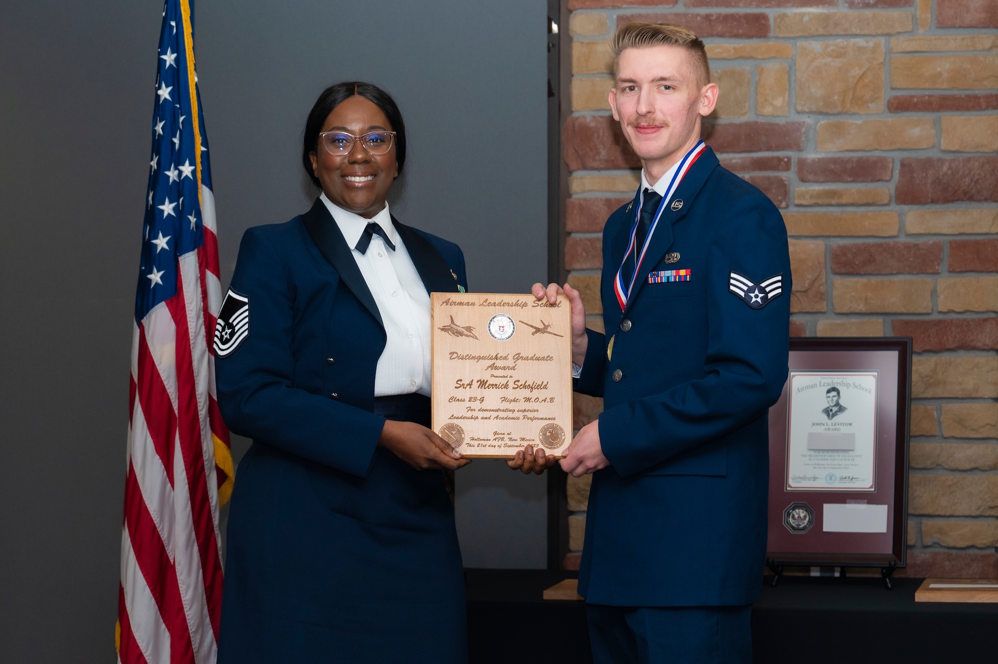 U.S. Air Force Senior Airman Merrick Schofield, right, Airman Leadership Graduate, accepts the Distinguished Graduate Award from Holloman Top III representative Master Sgt. Deshona Crowder during the graduation of MAYO ALS Class 23-G at Holloman Air Force Base, New Mexico, Sep. 21, 2023. The distinguished graduate award is presented to the top 10% of graduates for their performance in academic evaluations and demonstration of leadership. (U.S. Air Force photo by Airman 1st Class Michelle Ferrari)