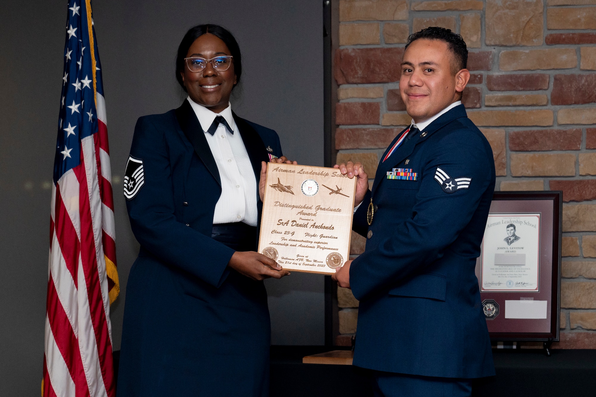 U.S. Air Force Senior Airman Daniel Anchodo, right, Airman Leadership Graduate, accepts the Distinguished Graduate Award from Holloman Top III representative Master Sgt. Deshona Crowder during the graduation of MAYO ALS Class 23-G at Holloman Air Force Base, New Mexico, Sep. 21, 2023. The distinguished graduate award is presented to the top 10% of graduates for their performance in academic evaluations and demonstration of leadership. (U.S. Air Force photo by Airman 1st Class Michelle Ferrari)