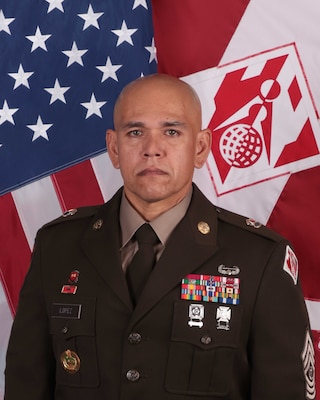 Photo of CSM Lopez posing in front of the national colors and Corps colors.