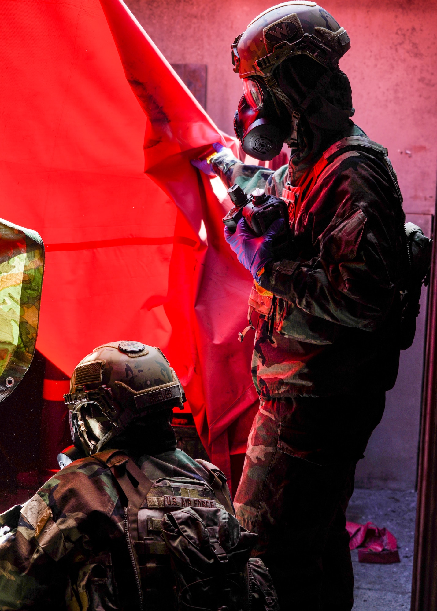 California Air National Guard Airmen dressed in chemical protection suits looking left off the frame of the image inside a fire department training area.