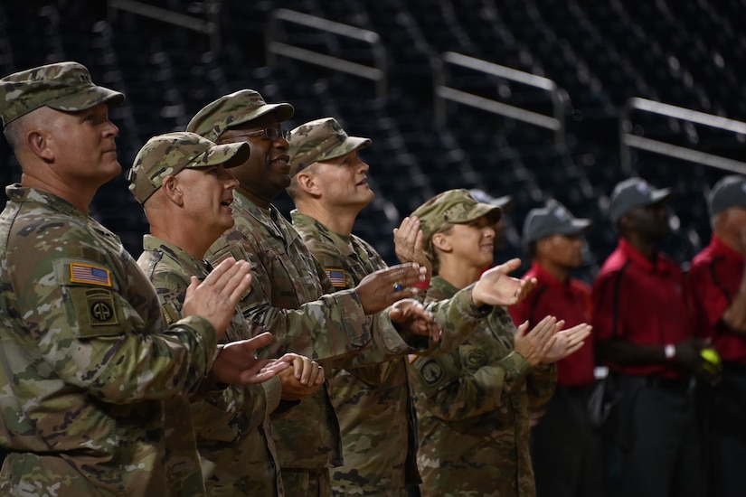 Military members are seen clapping while on the Nationals Park pitch. Referees for the game are also standing together and are seen in the background.