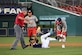 A Joint Base Andrews softball player is seen laying on a base while a catcher from the other team is seen catching a softball.