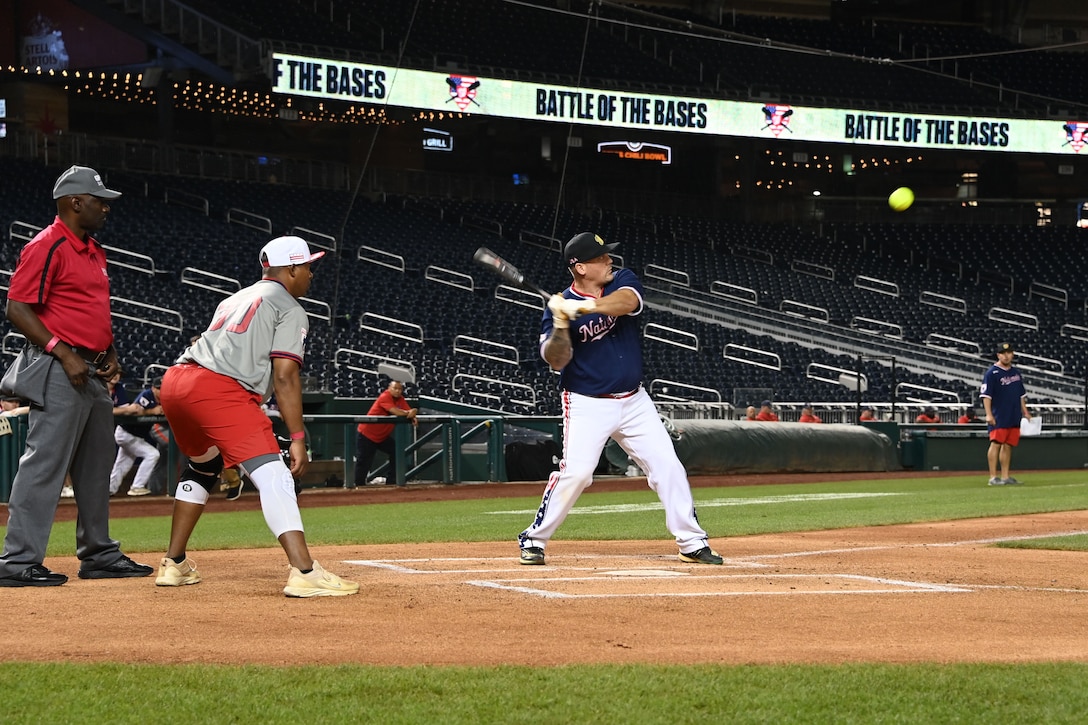 A Joint Base Andrews softball player is swinging his bat to hit a softball that is seen coming towards him.