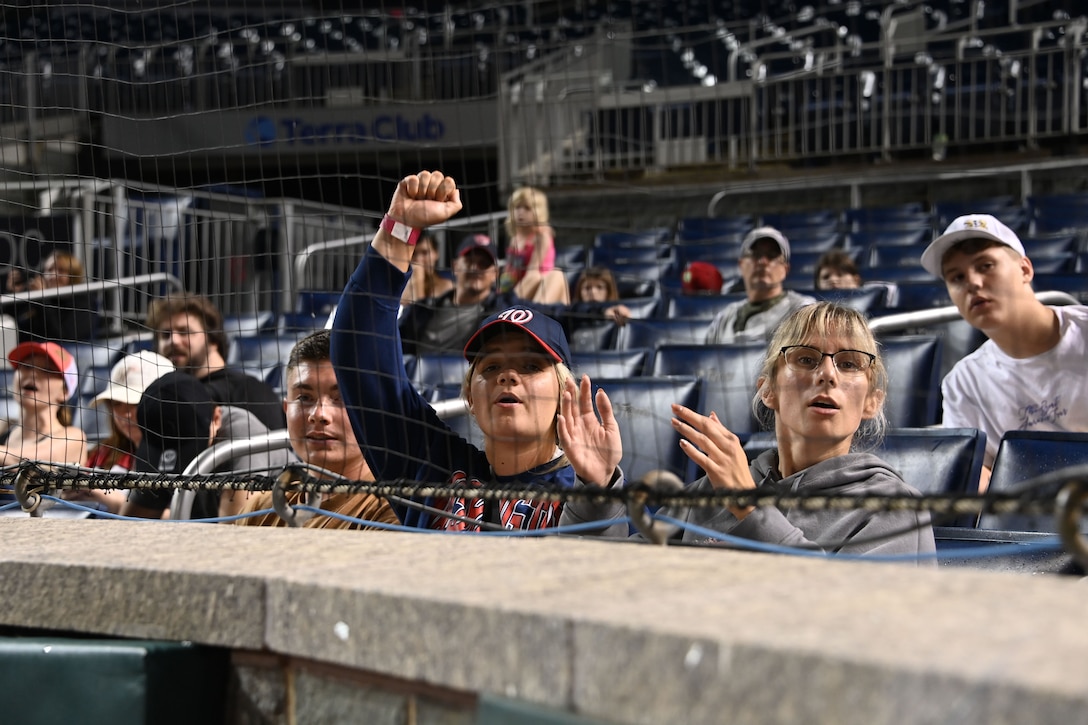 Fans sitting in the stands cheer for the softball team.